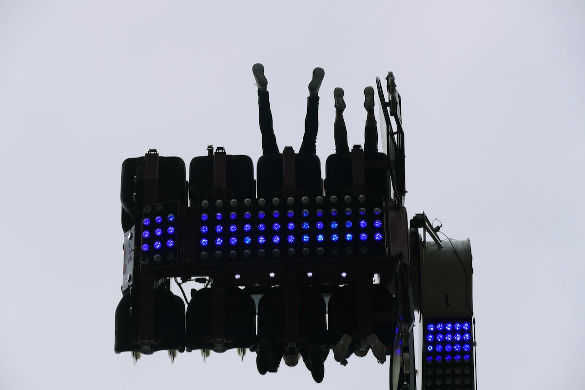 Looking up at the underside of a fairground thrill ride, with people's feet sticking out