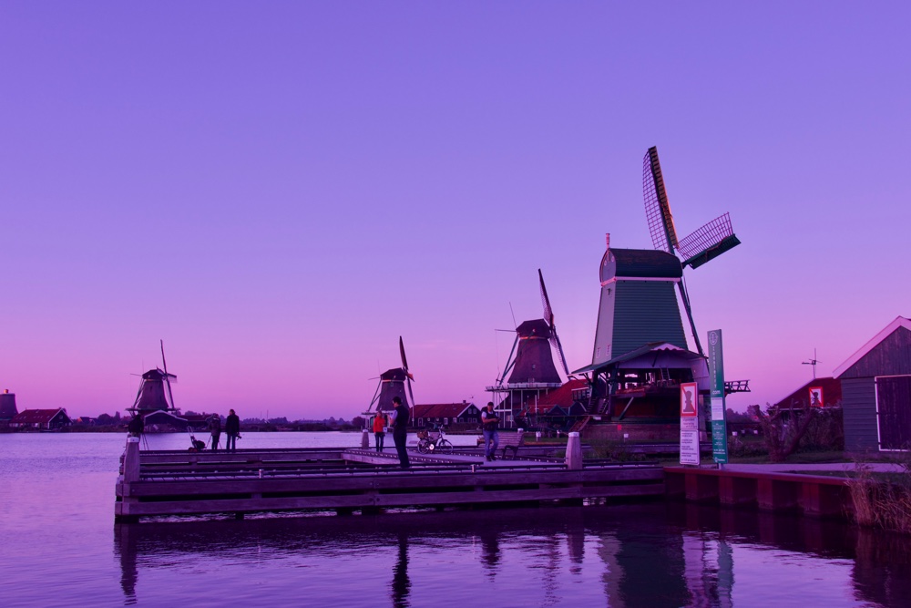 Zaan river at Zaanse Schans. Windmills in the background, and people on a jetty in the foreground.