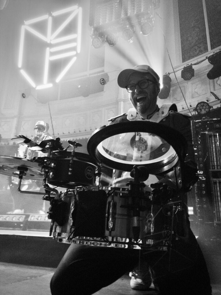 Close-up of Meute's marching band drum player, kneeling down, playing drums, and grinning happily