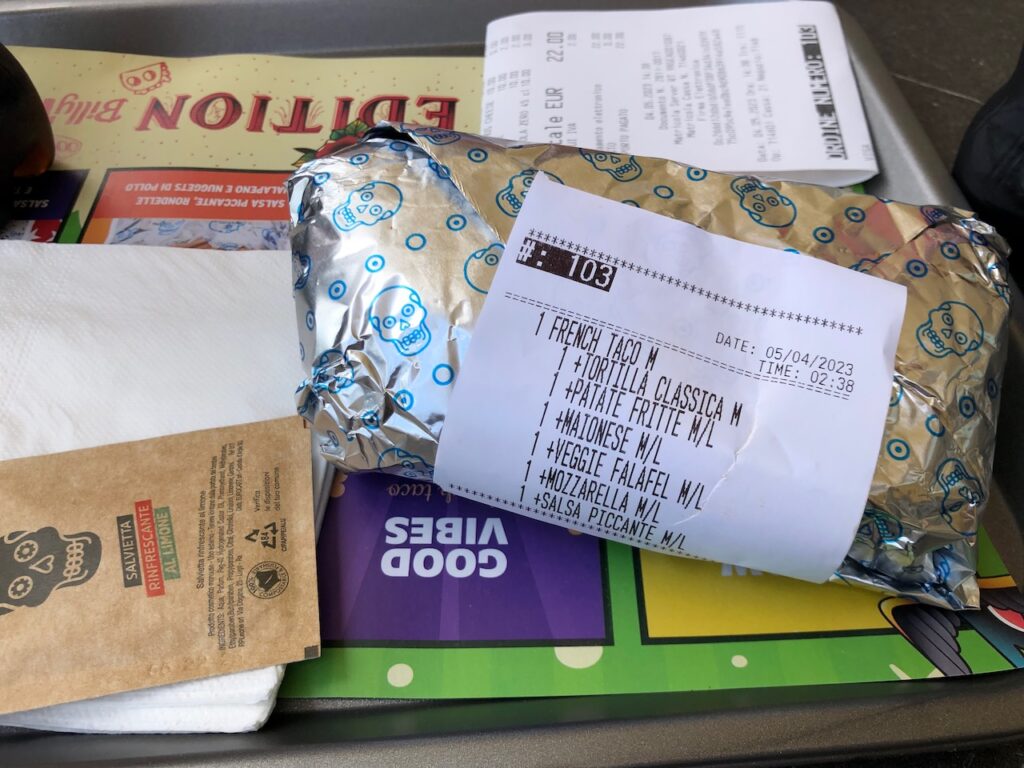 A Billy Tacos tray, with on it my French Taco, wrapped in alumimium foil. The receipt is attached to it. The recieipt shows the ingredients: tortilla, french fries, mayonaise, falafel, mozzarella, spicy salsa.